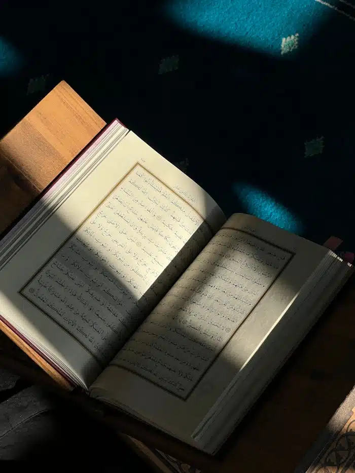 An open book with Arabic script is bathed in sunlight on a wooden table.
