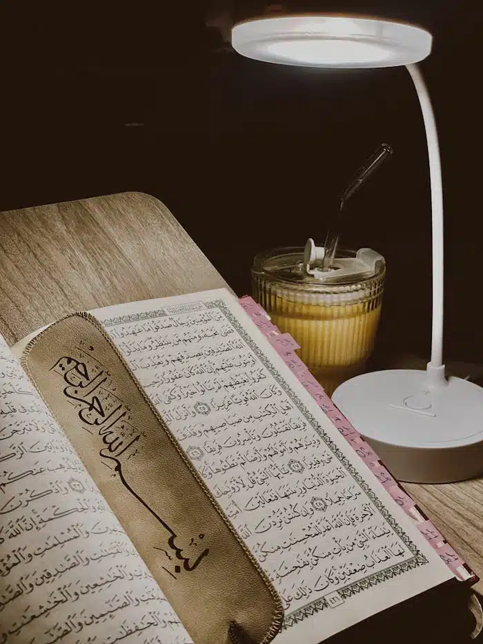 Open Quran with bookmark under a lamp, creating a serene reading ambiance.