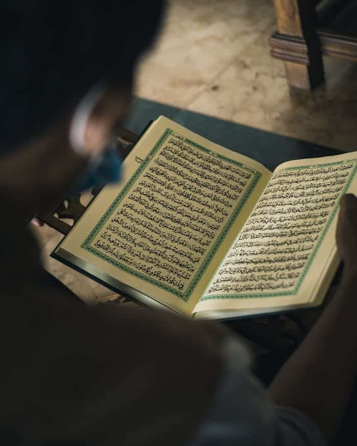 our-story A thoughtful moment of a Muslim man reading the Quran indoors, capturing faith and spirituality.